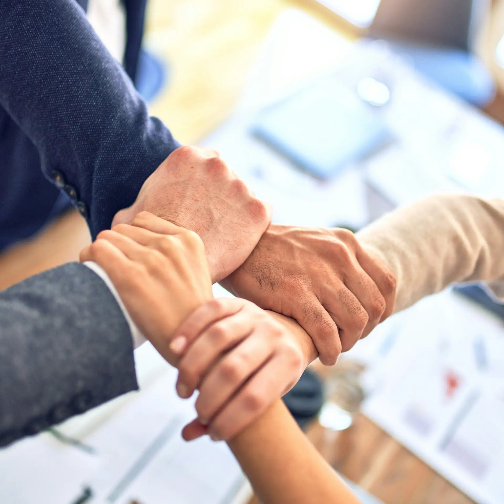 Four people joining hands together in a circle over a table.