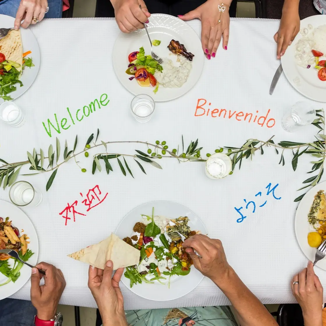 People sharing a meal with welcome greetings in multiple languages.