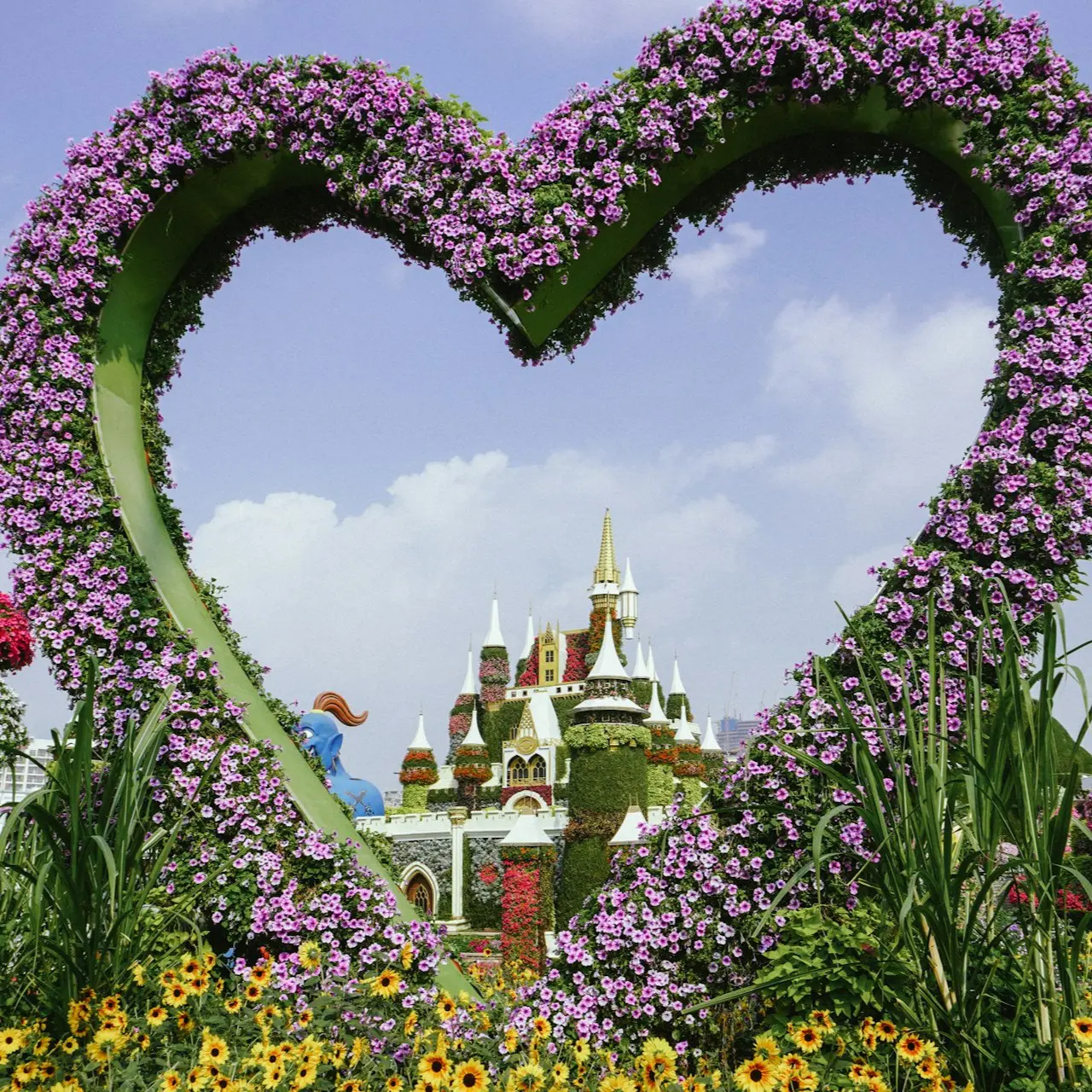 Floral heart-shaped arch framing a flower-covered fairytale castle under a blue sky.