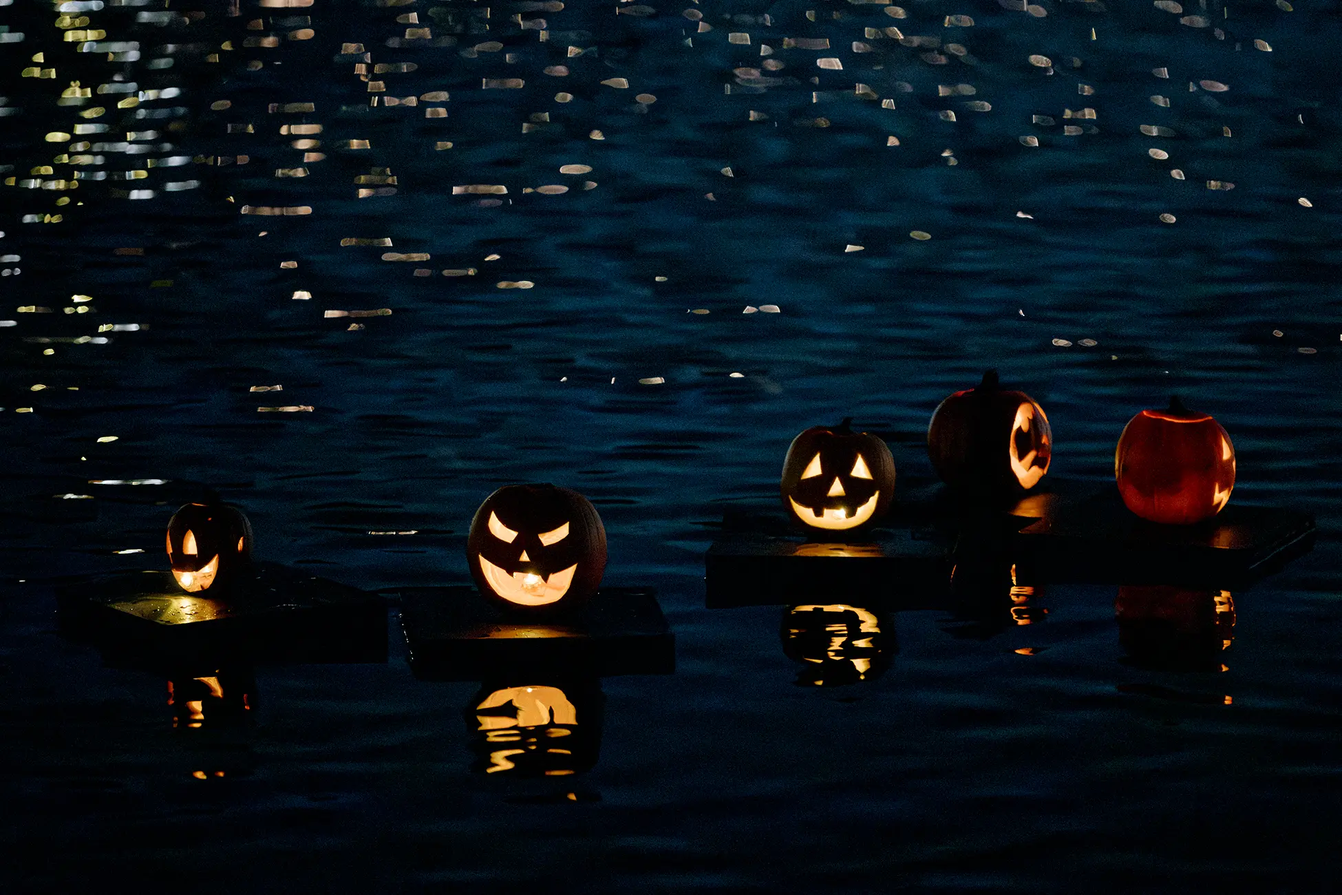 Five illuminated jack-o'-lanterns floating together on the lake